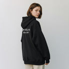 The JeJe Korea fashion&lifestyle ADLV X HOSHI 블랙 코튼 와펜 후드티를 입고 뒤를 돌아보는 모델